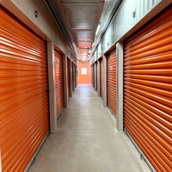 A long hallway with orange doors and concrete floors.